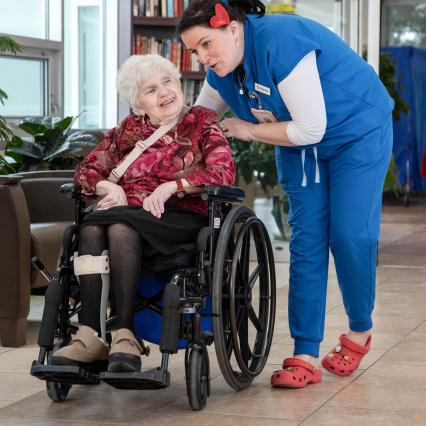 Continuing care worker pushing a patient in a wheelchair leaned over having a conversation